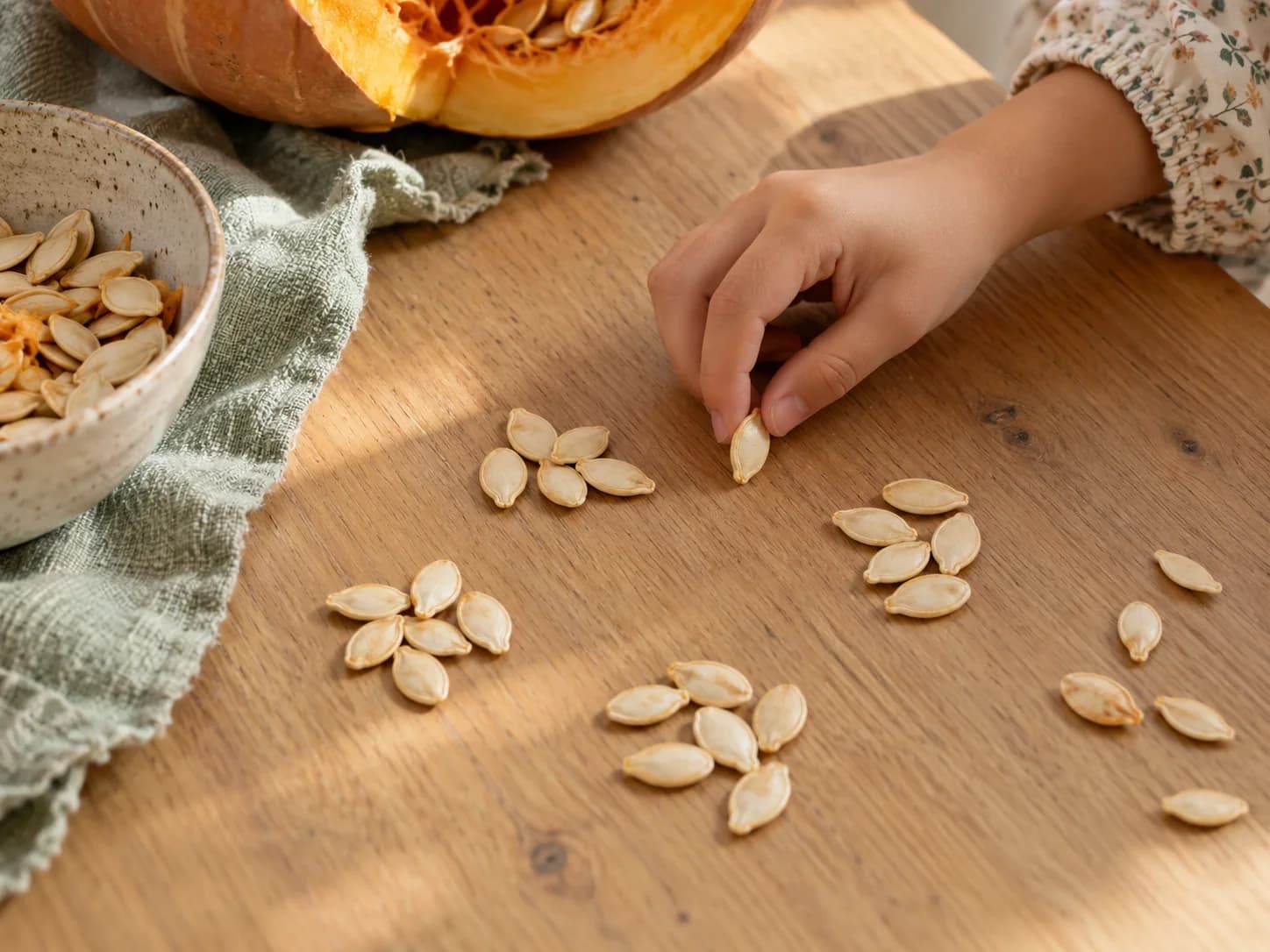 A child moves a pumpkin seed between small groups of seeds on a wooden table.