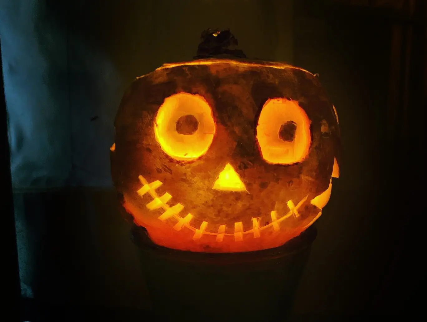 A turnip lantern glowing in the dark with round eyes, a small triangular nose, and a stitched grin.