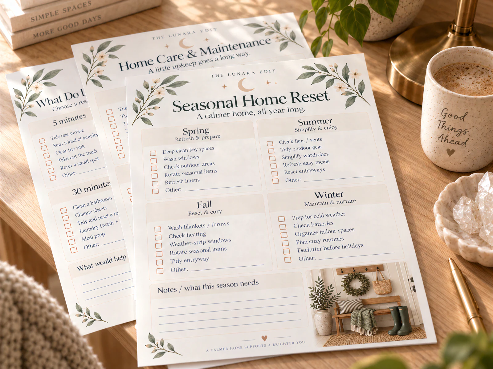 The Seasonal Home Reset page, with spring, summer, fall, and winter checklists, lying on top of the Home Care & Maintenance and What Do I Have in Me Today? pages on a sunlit wooden desk with a mug and a brass lamp